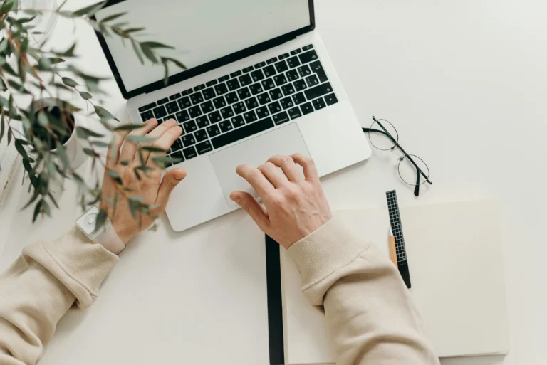 La mano de una persona utilizando una computadora portátil mientras trabaja en un empleo online.